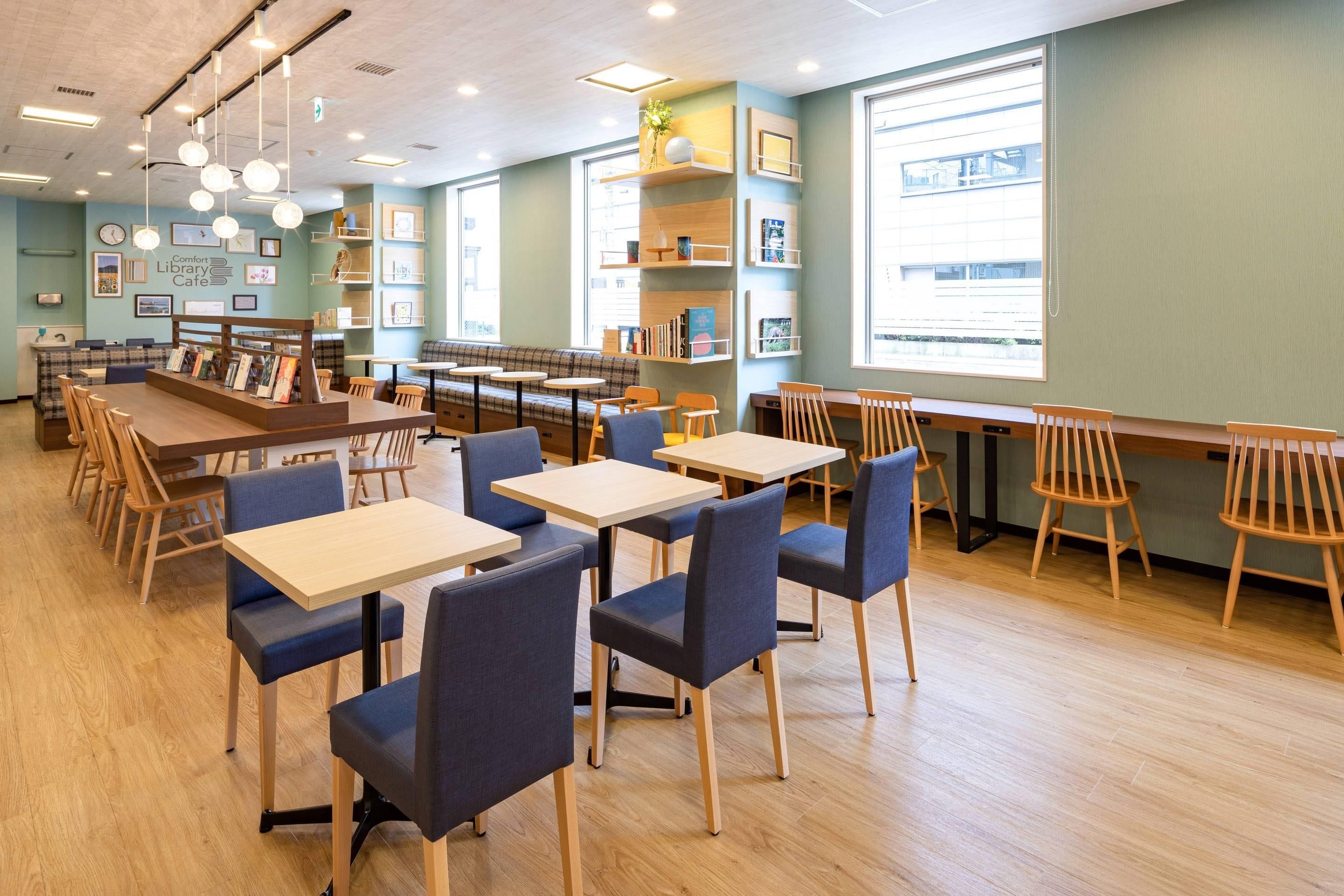 A library cafe with tables and chairs, bookshelves, and a large window.