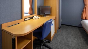Une chambre d’hôtel avec un bureau en bois, un écran d’ordinateur, un téléphone, une chaise bleue, une armoire et un lit avec des rideaux.