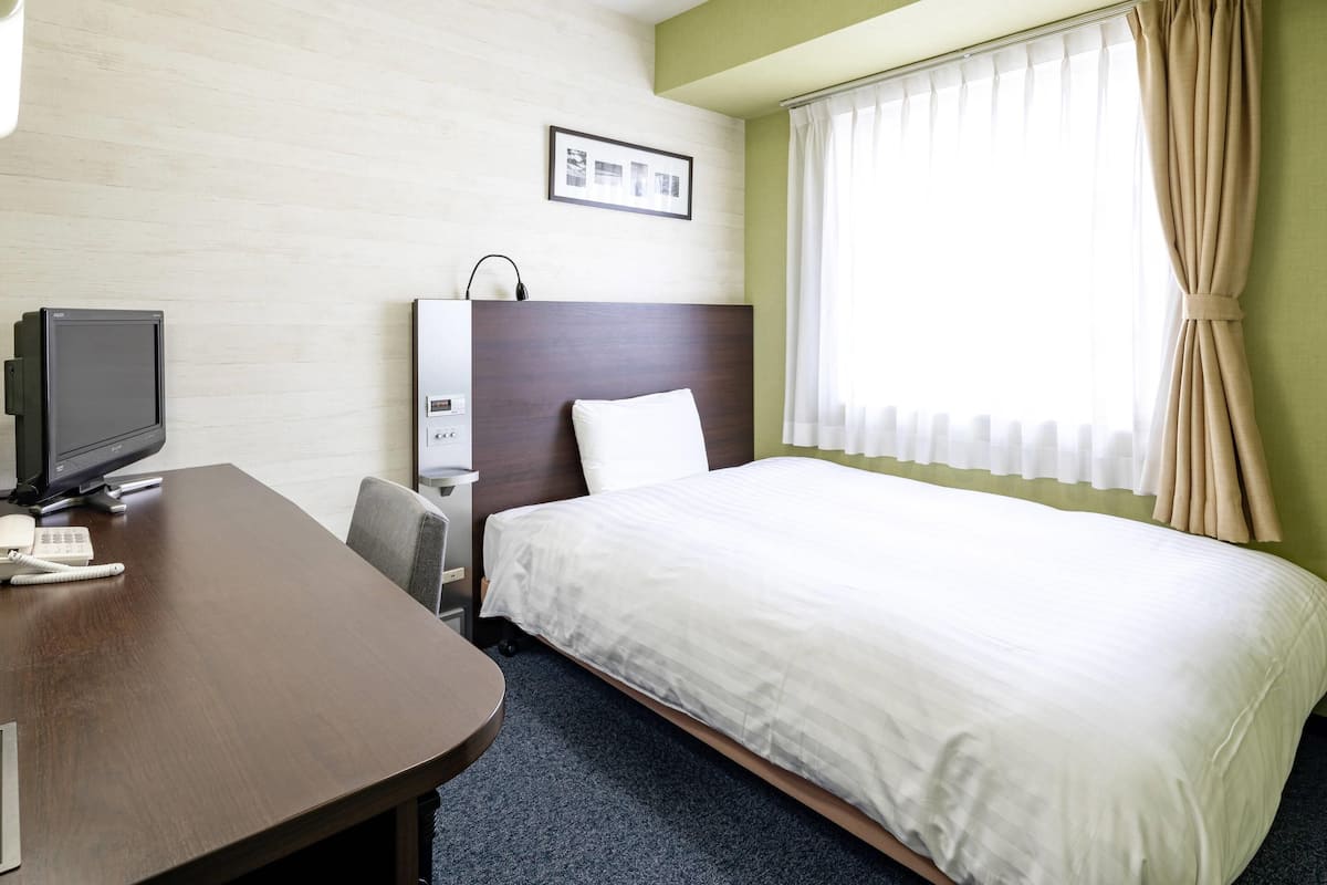 Ein Hotelzimmer mit einem Bett, einem Schreibtisch mit Bildschirm, einem Telefon und einem an der Wand montierten Fernseher.