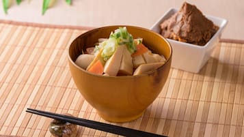 Un tazón de tofu y verduras sobre un tapete de bambú, con palillos y un recipiente pequeño de pasta de miso.