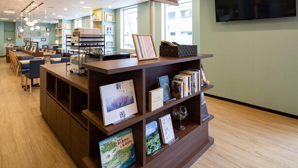 Un café-bibliothèque avec des étagères en bois où sont exposés des livres et des photos encadrées, un comptoir avec une machine à café et un grand téléviseur fixé au mur.