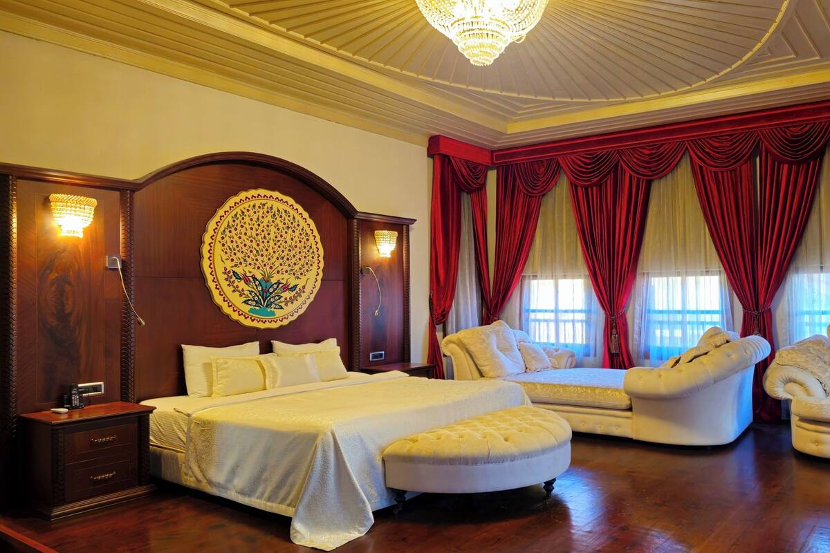 A luxurious bedroom with a large bed, a chaise lounge, and a sitting area.