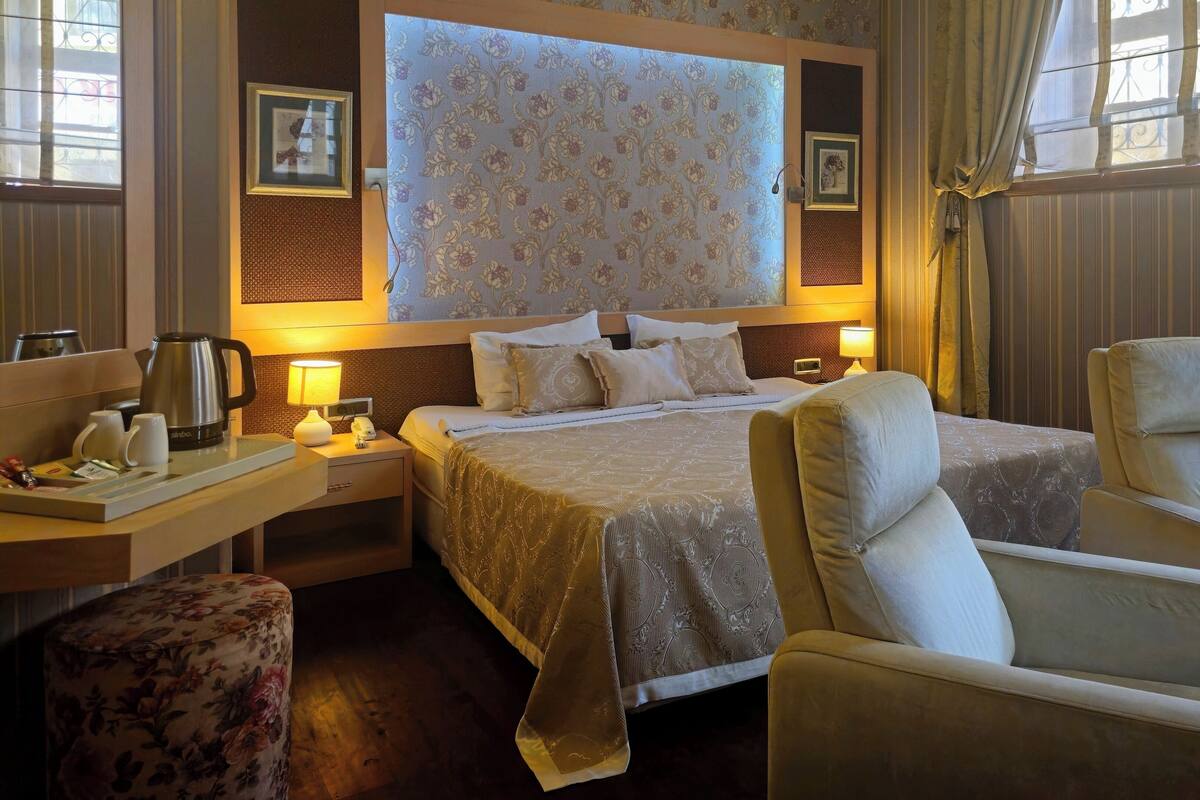 A hotel room with a bed, two bedside tables, a chair, a coffee maker, and a window with curtains.
