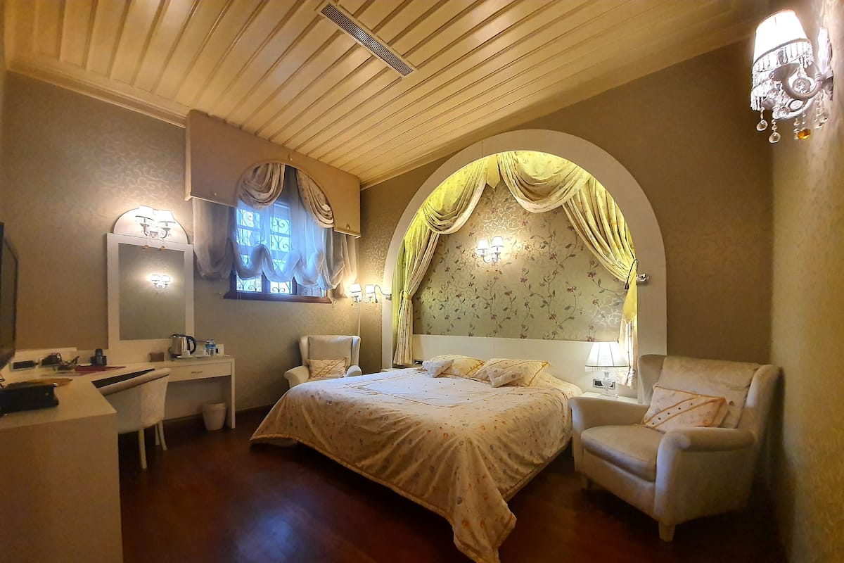 A bedroom with a large bed, a desk, a chair, and a vanity.
