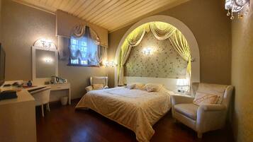 A bedroom with a large bed, a desk, a chair, and a vanity.