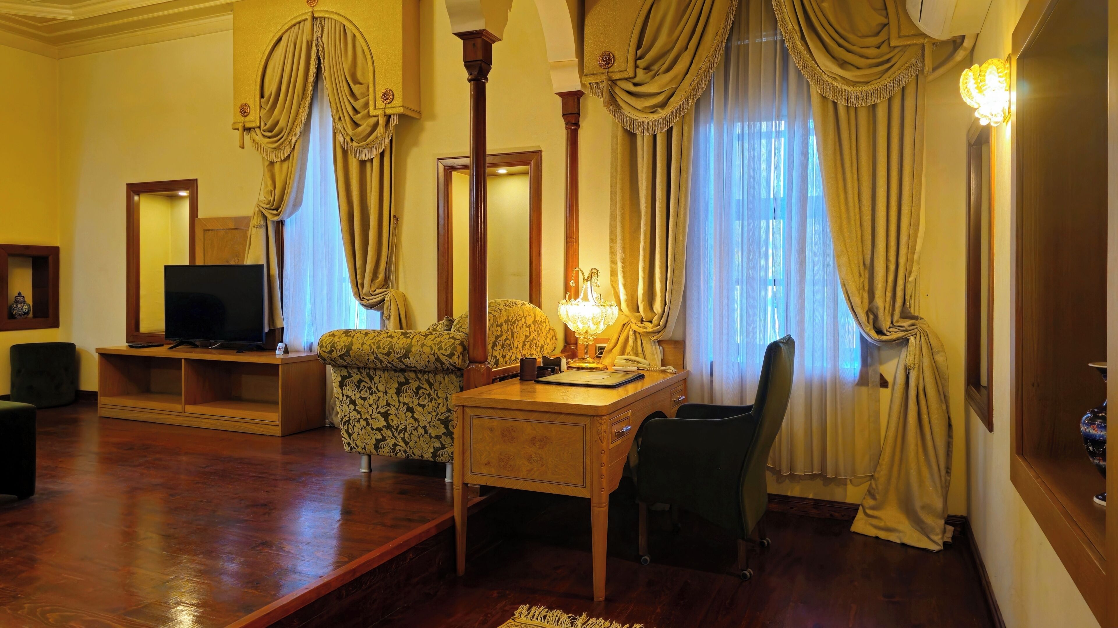 A room with a wooden desk, a television, a patterned sofa, and a chair.