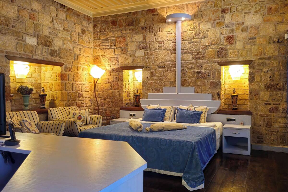 A bedroom with a stone wall, a bed with blue bedding, two bedside tables, and a floor lamp.
