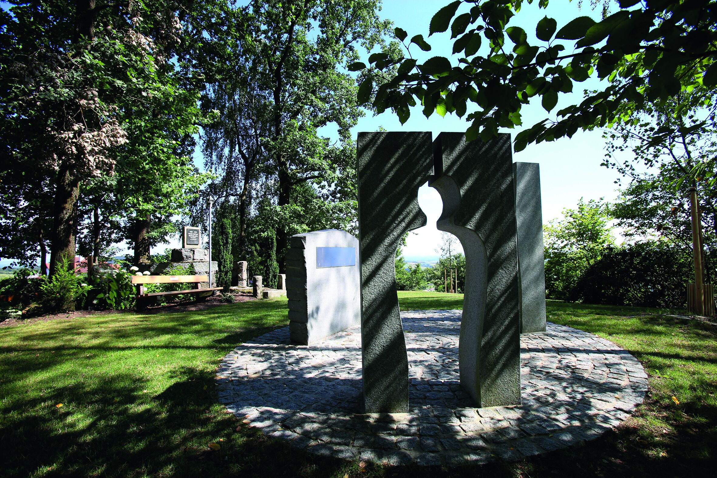 Eine Steinskulptur mit einem Bogen in einer Parkanlage.