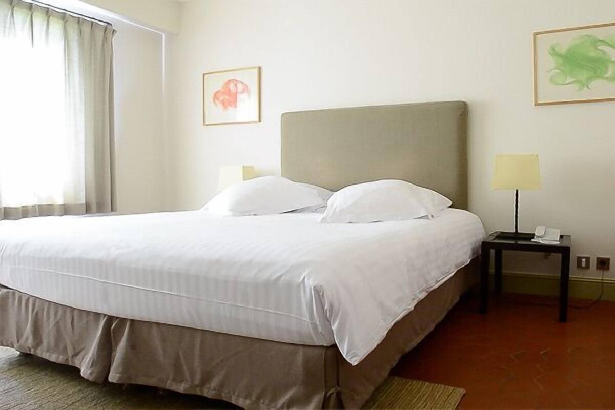 Una habitación de hotel con cama, una silla, una mesita de noche y dos lámparas de pared.