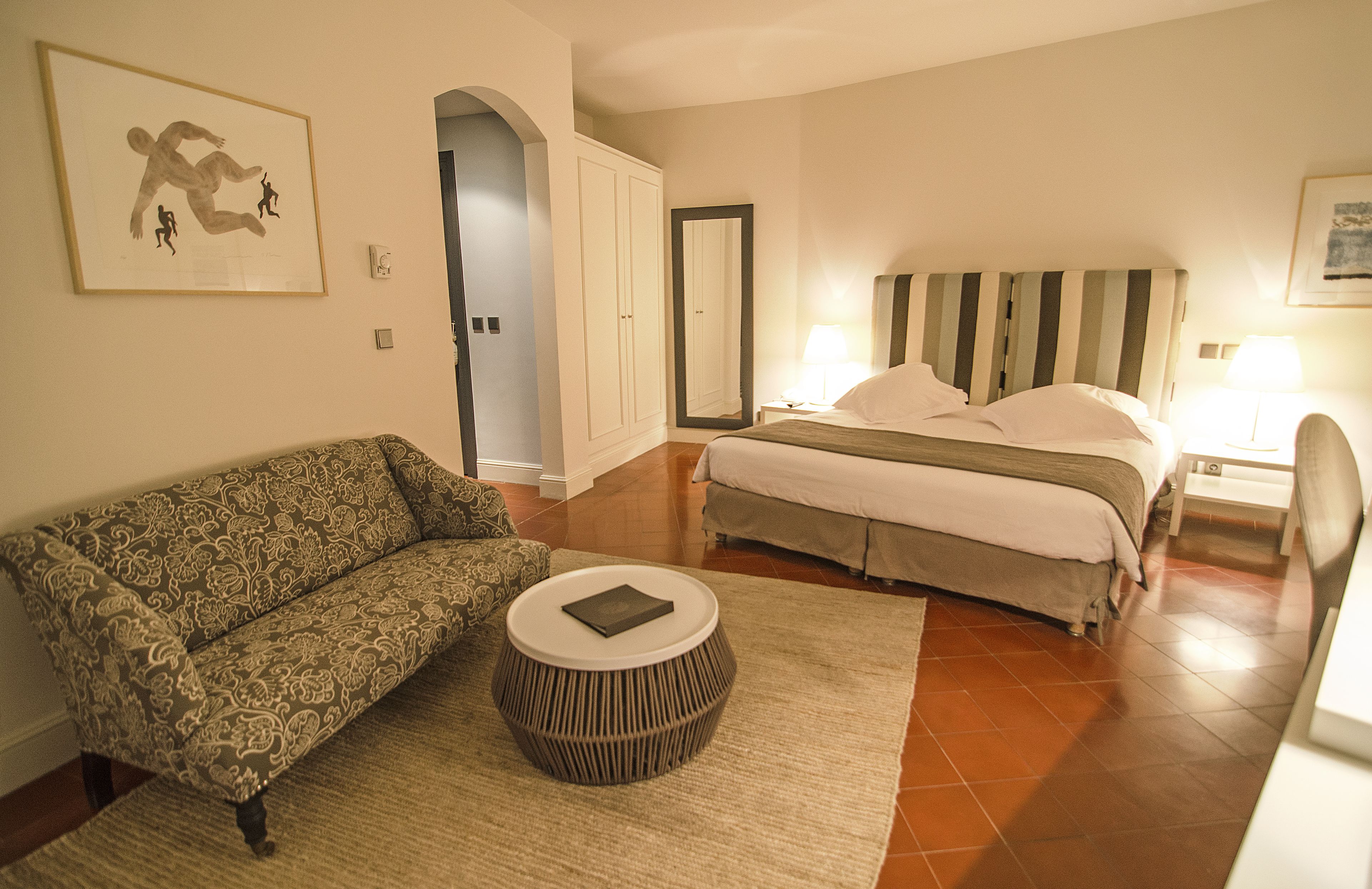 A bedroom with a bed, a sofa, a round coffee table, and a framed picture on the wall.