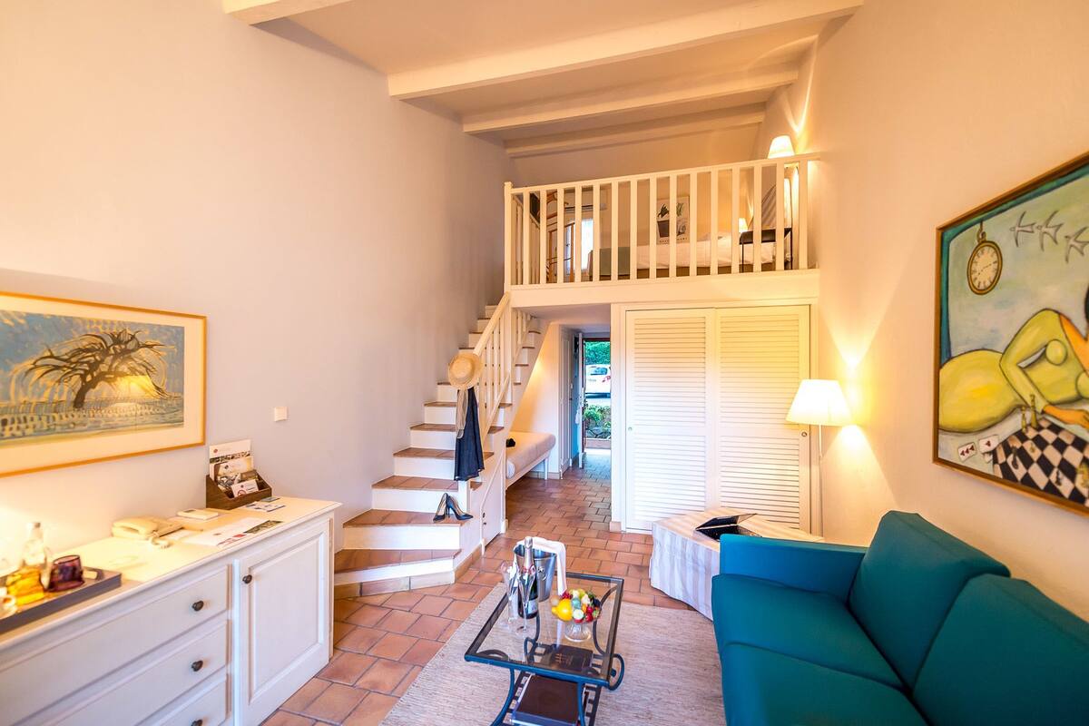 Un vaste espace de vie comprenant un escalier menant à un balcon, un canapé, une table basse et un tableau accroché au mur.