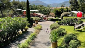 A garden pathway leading to outdoor seating areas with umbrellas, surrounded by well-maintained hedges and plants.