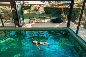 A swimming pool with clear water, surrounded by a glass enclosure, and a patio area with outdoor furniture. - Hotel Spa & Restaurant Cantemerle (Vence)