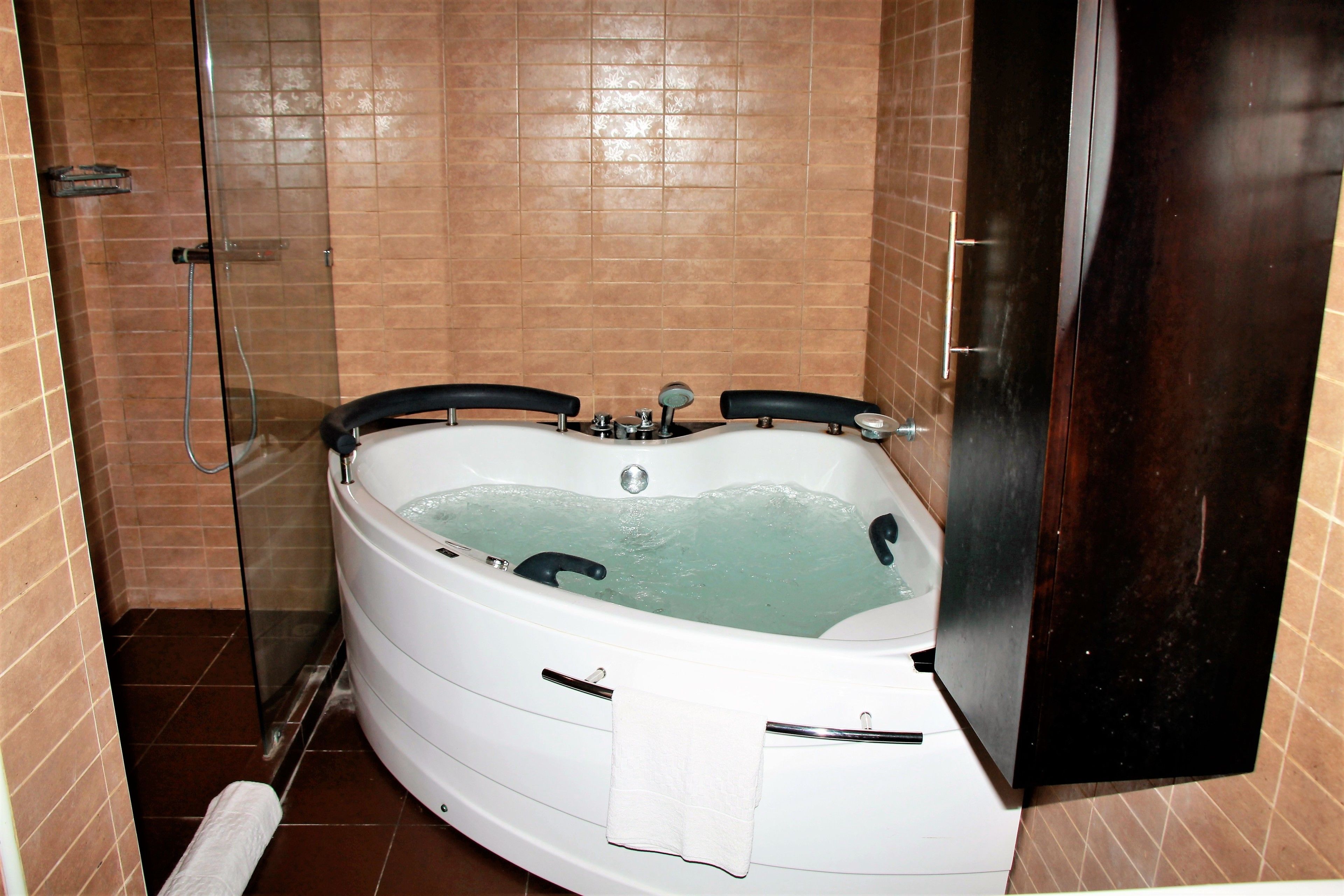 A bathroom with a large bathtub, a glass shower enclosure, and a dark wooden cabinet.