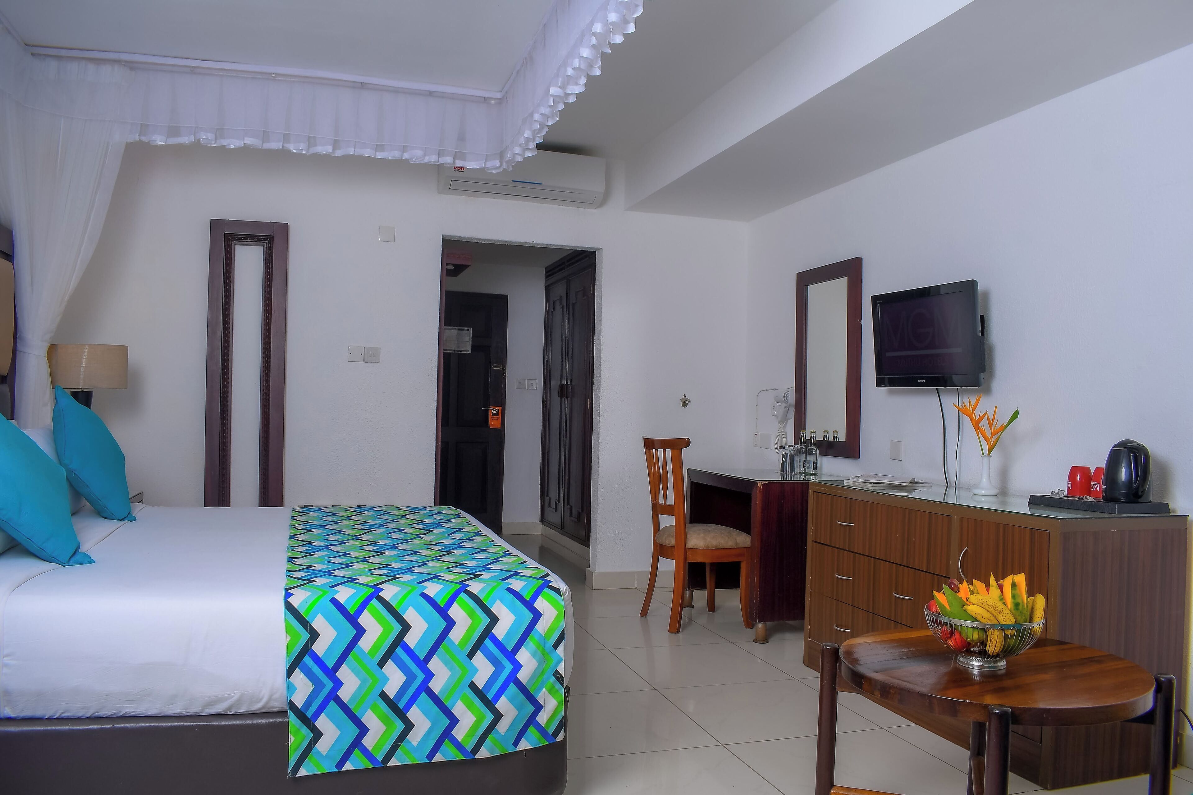 A hotel room with a bed, a desk, a chair, a television, and a bowl of fruit on the desk.