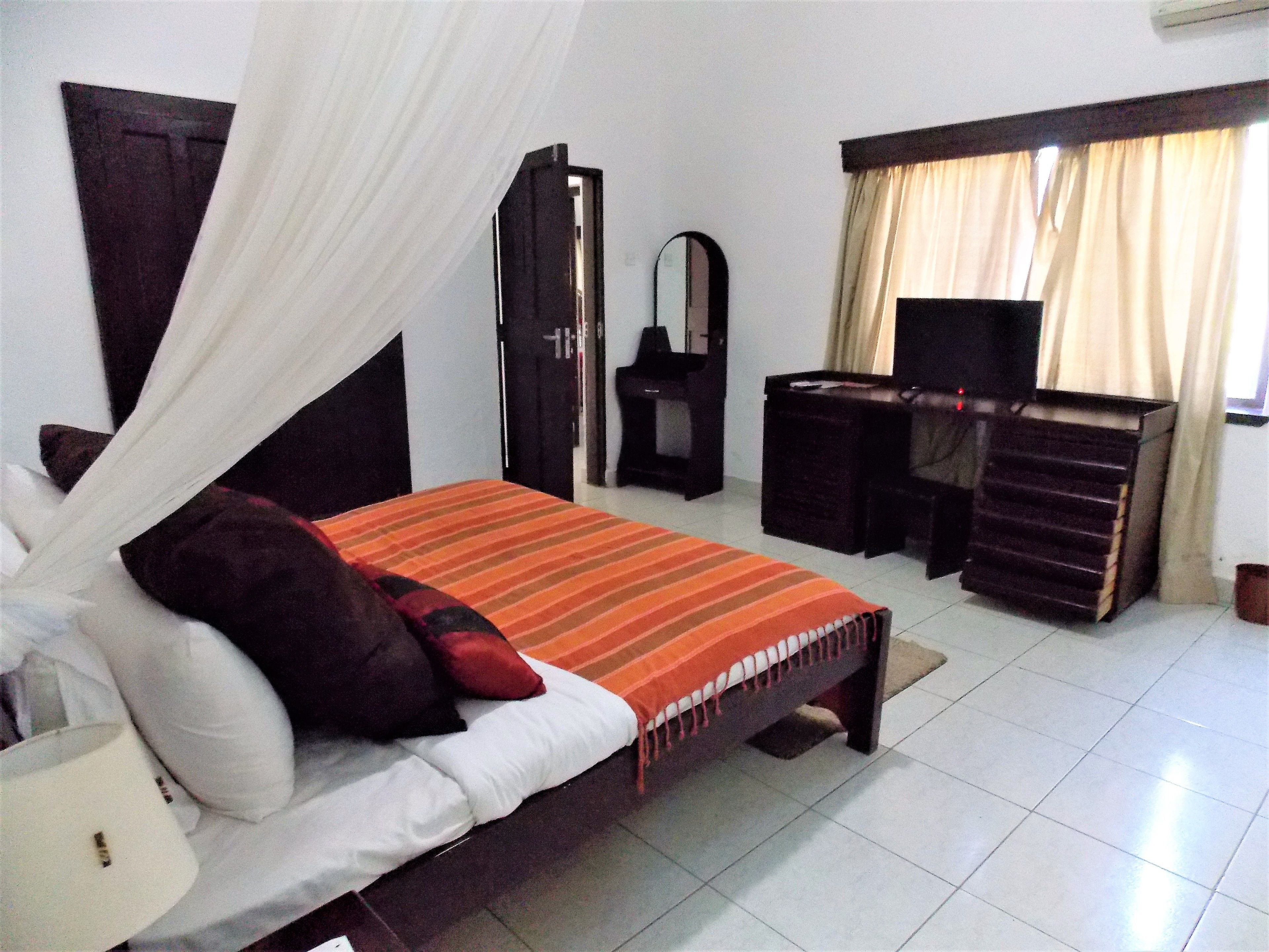 A bedroom with a bed, a desk, a chair, a mirror, and a television.