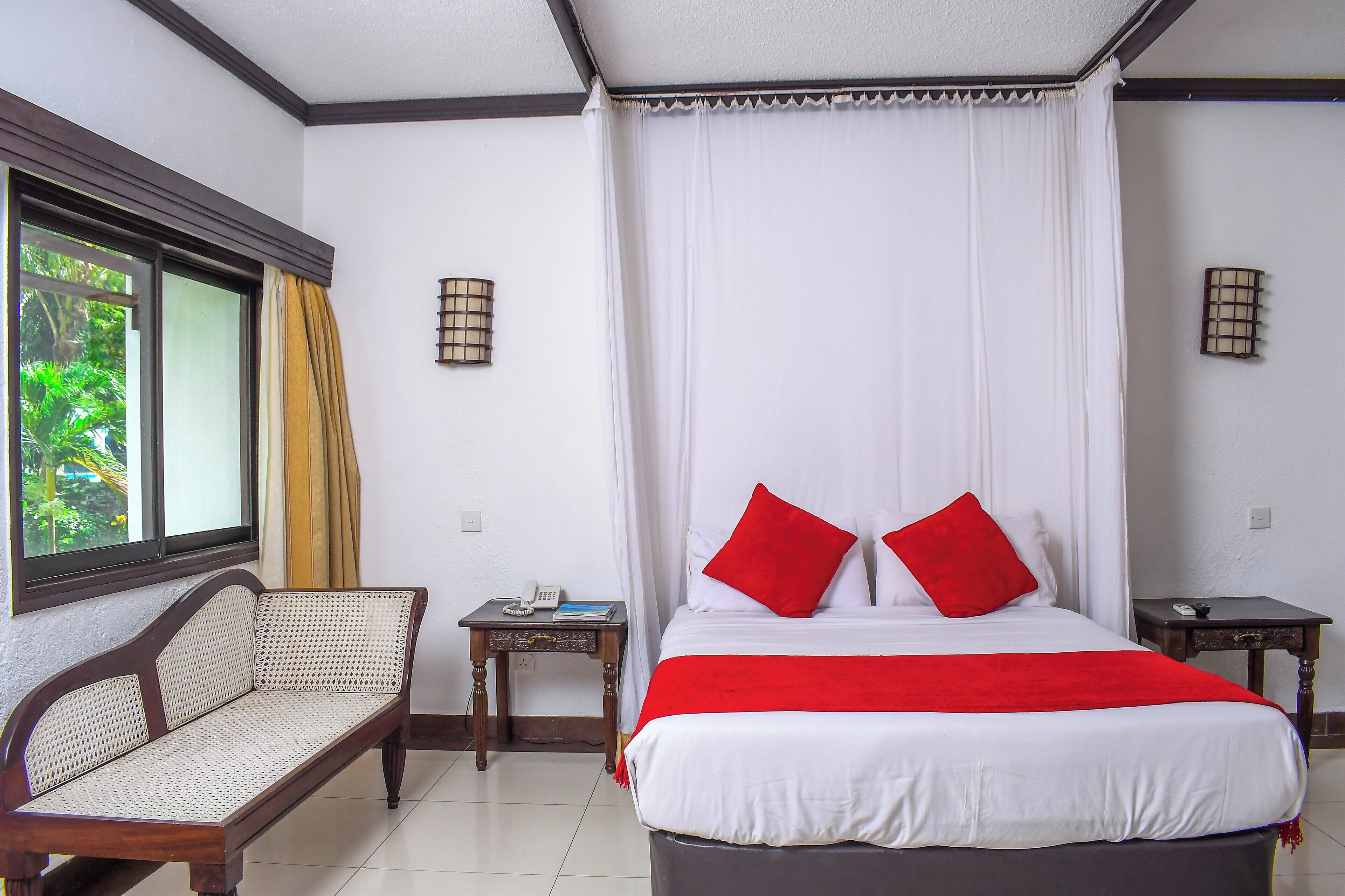 Un dormitorio con una cama, un sofá, dos mesitas de noche y una ventana con cortinas.