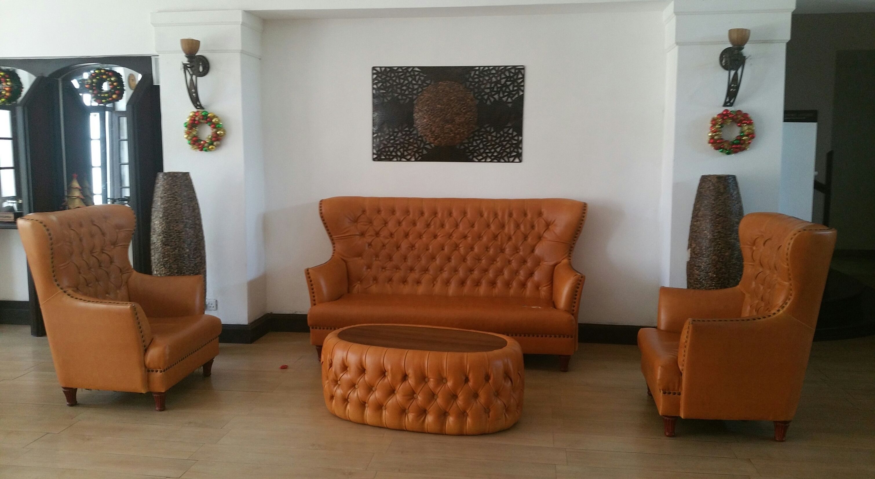 Een woonkamer met een bruine leren bank, twee bijpassende fauteuils en een rond pouf.