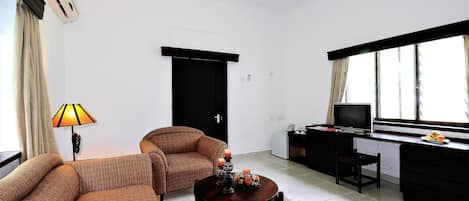 A living room with a sofa, a coffee table, a lamp, a TV, and a desk with a computer.