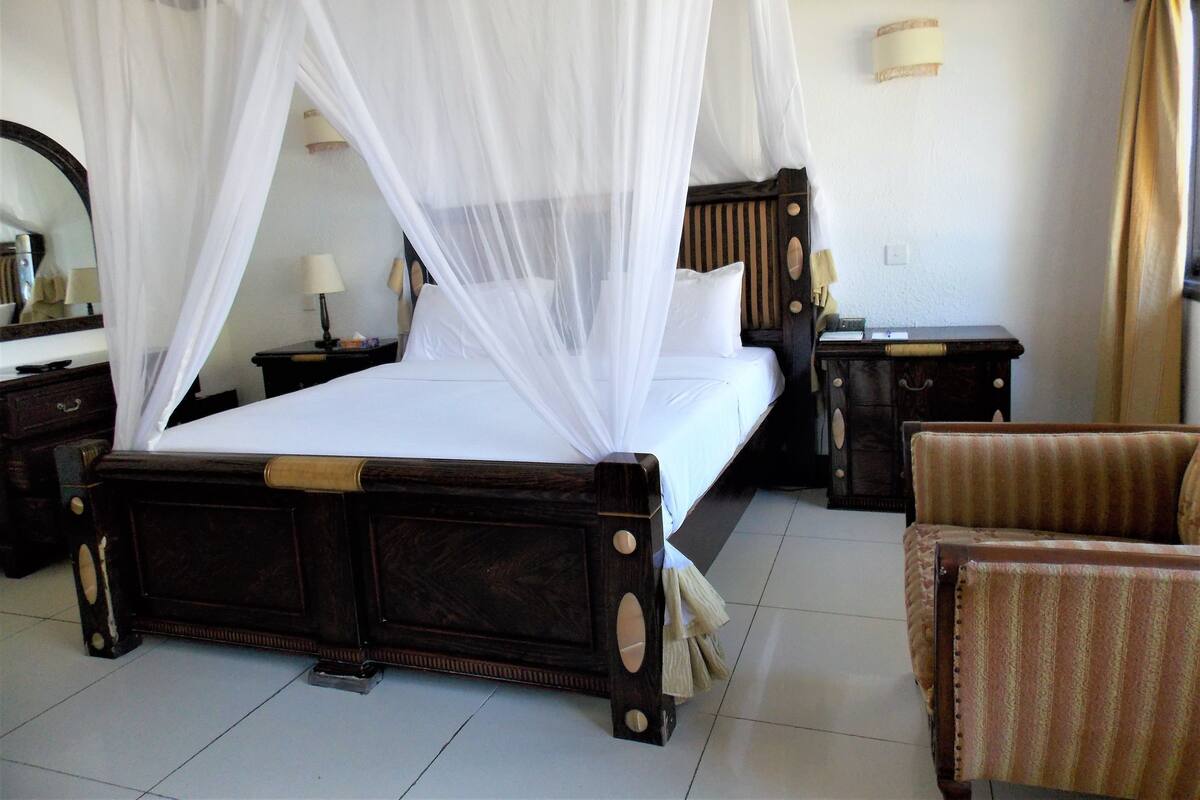 Une chambre d’hôtel avec un lit à baldaquin, une table de chevet, une chaise et une petite table.