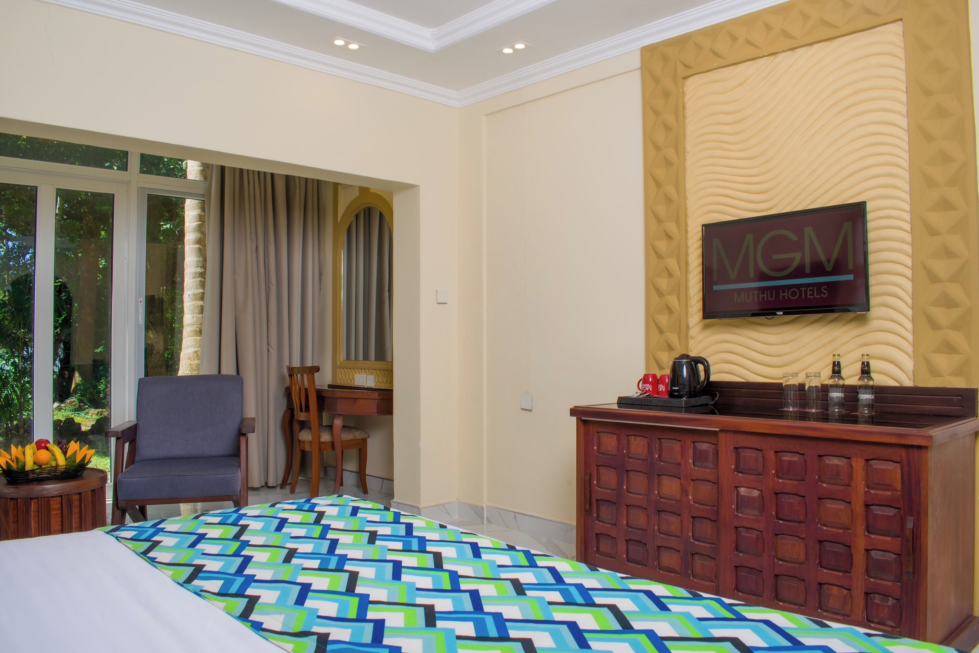 Una camera d'albergo con un letto, una scrivania, una sedia, un minibar e una grande finestra.