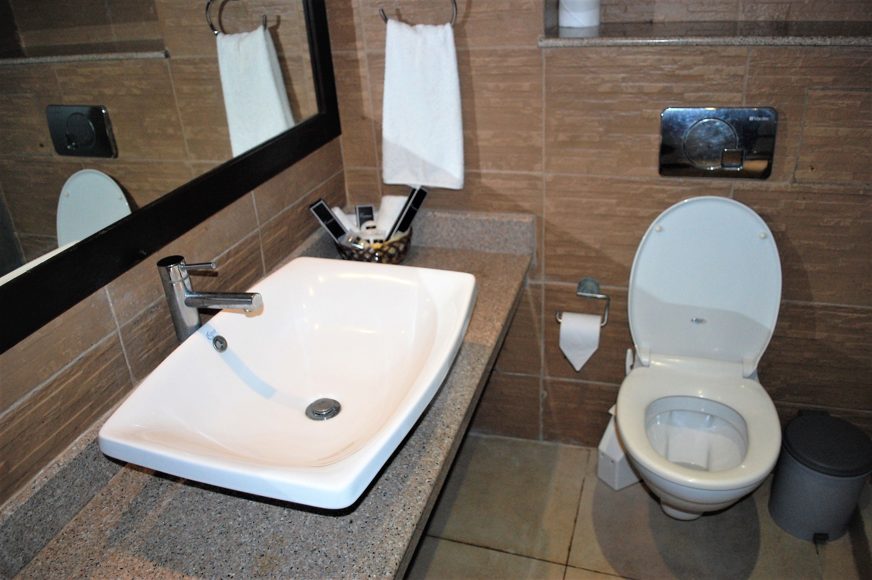 Une salle de bain avec un lavabo blanc, un miroir, des toilettes et une poubelle.