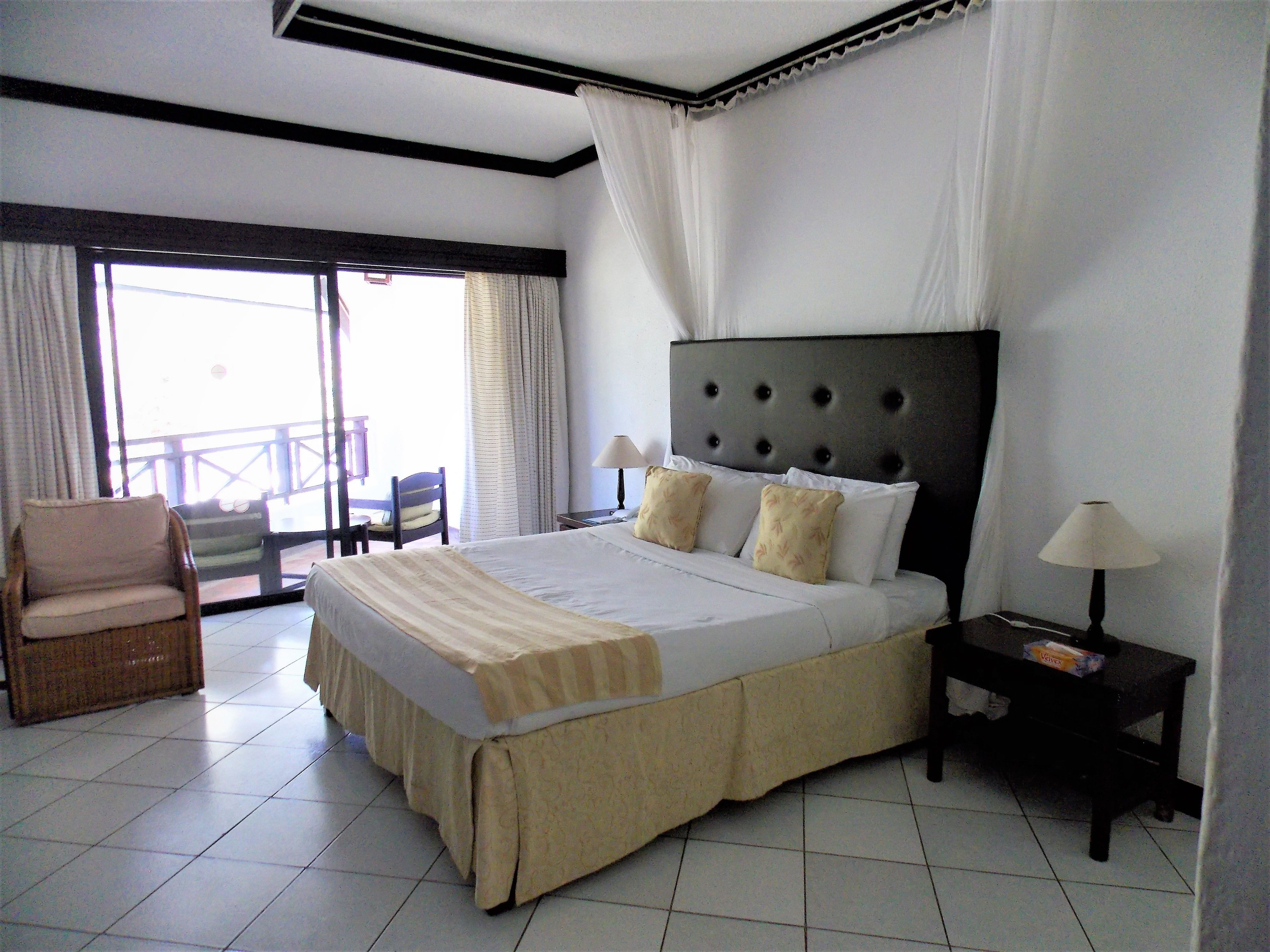 Habitación de hotel con una cama grande, una silla, una mesita de noche y vistas al exterior.