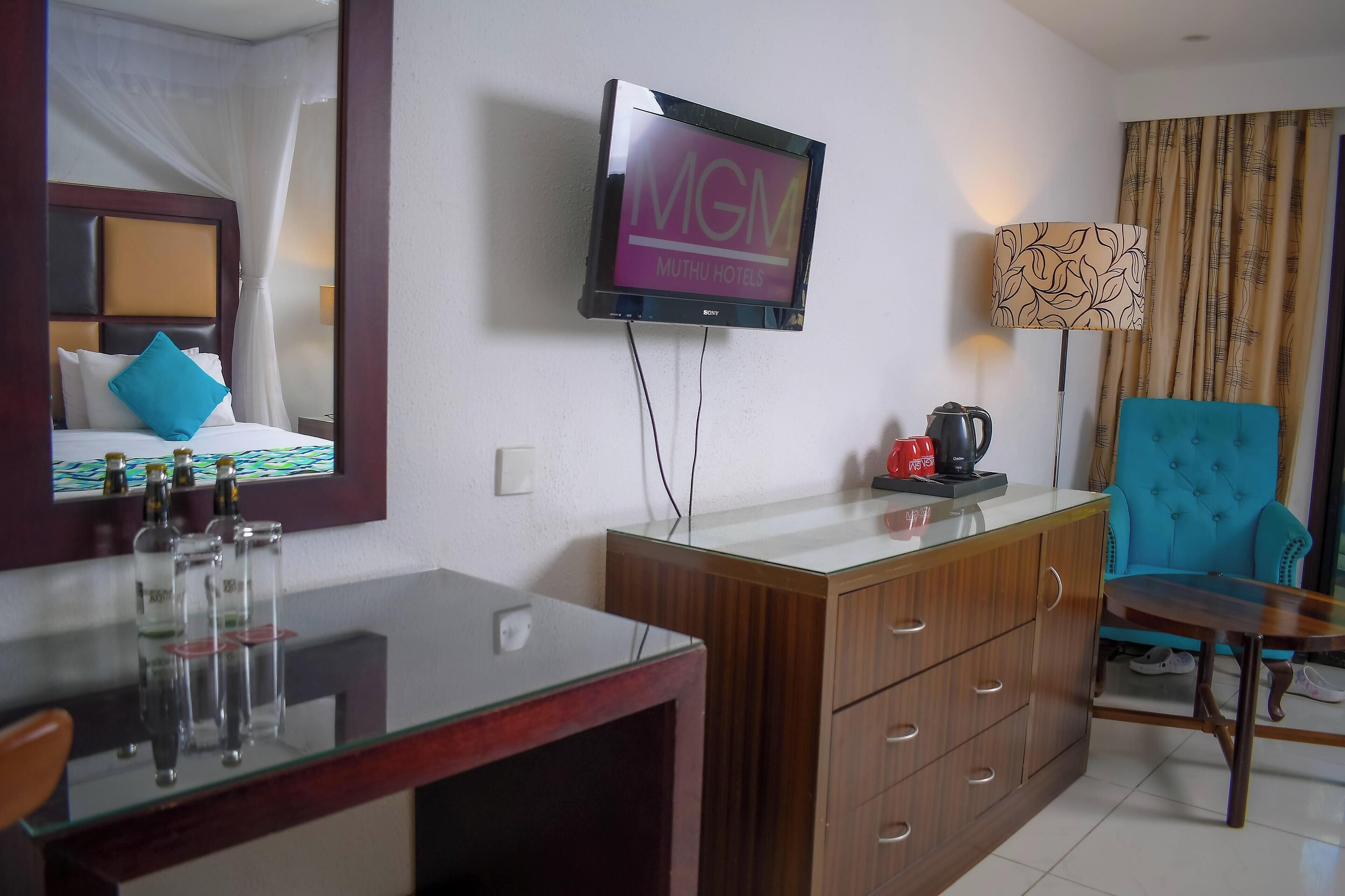 Habitación de hotel con cama, televisor montado en la pared, escritorio con lámpara y una silla.