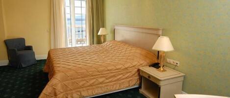 A hotel room with a bed, bedside tables, a chair, and a view of the outdoors.