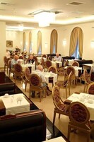 Un comedor con mesas y sillas redondas, una barra larga y una línea de buffet.