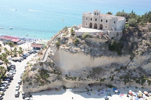 A coastal building with a balcony overlooking the sea, a parking area, and a beach with umbrellas. - Hotel Villa Antica (Tropea)
