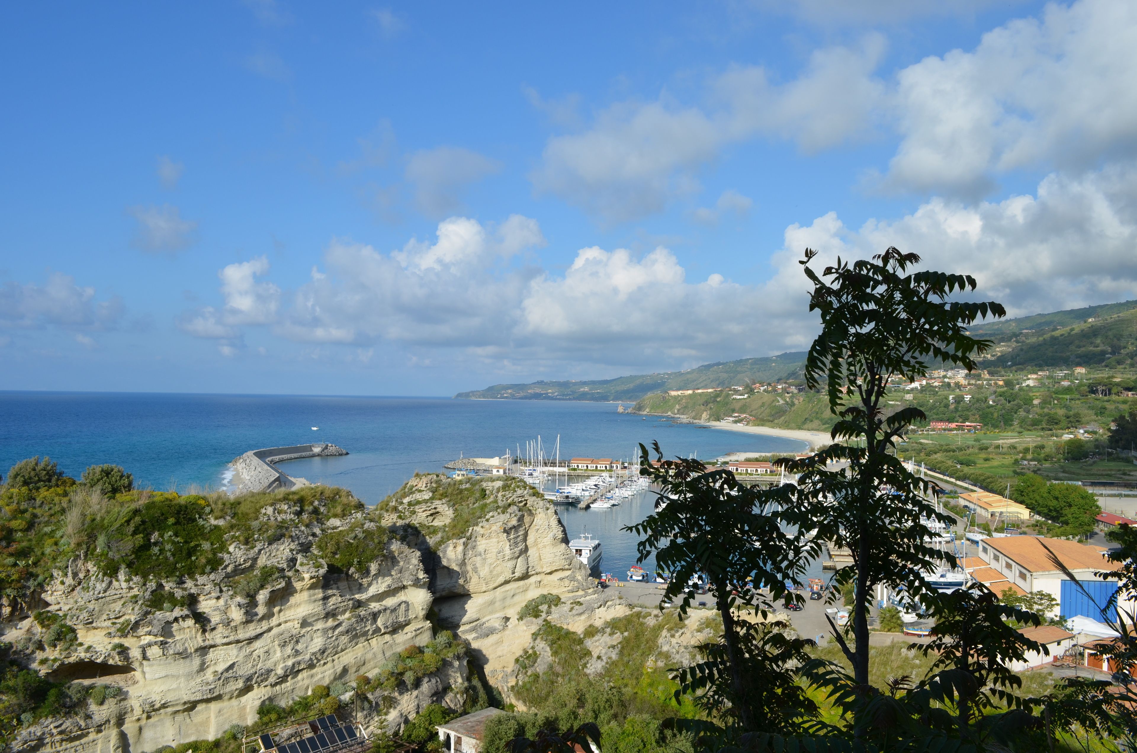 A coastal town with rocky cliffs, a marina with boats, and a clear blue sky.