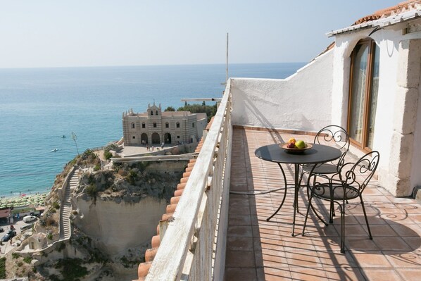 Balcón con mesa y sillas con vistas a la costa, un edificio histórico y una vista despejada del mar.