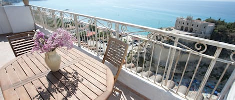 A wooden table with a vase of flowers on a balcony overlooking a coastal view.