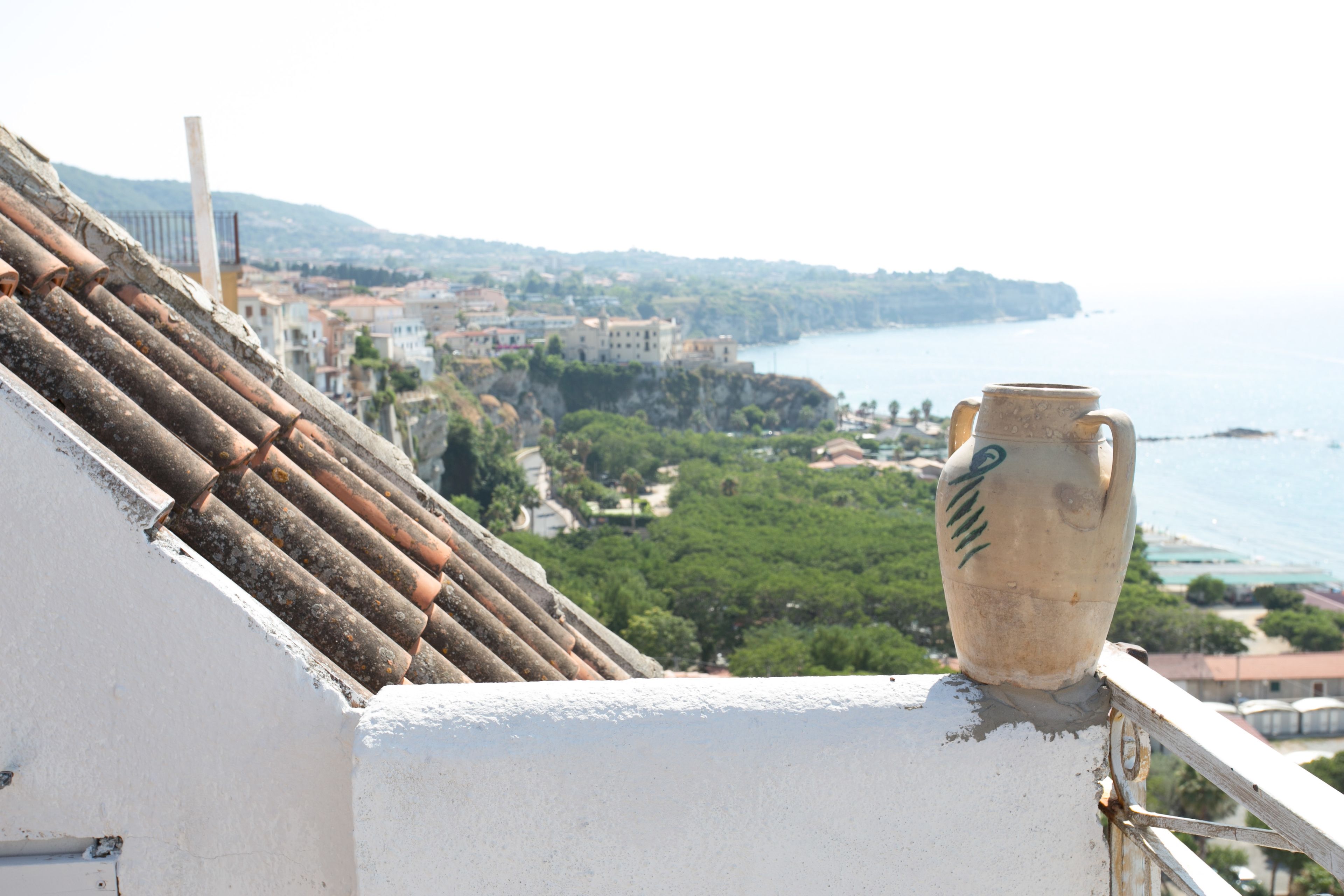 A white building with a tiled roof and a vase on the balcony railing.
