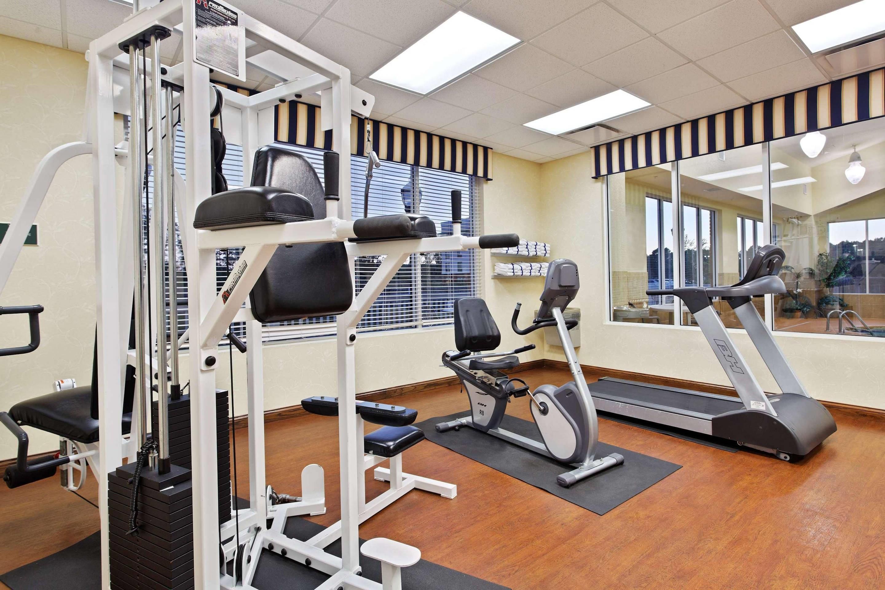 A gym with exercise equipment, a treadmill, and a mirror reflecting the room.