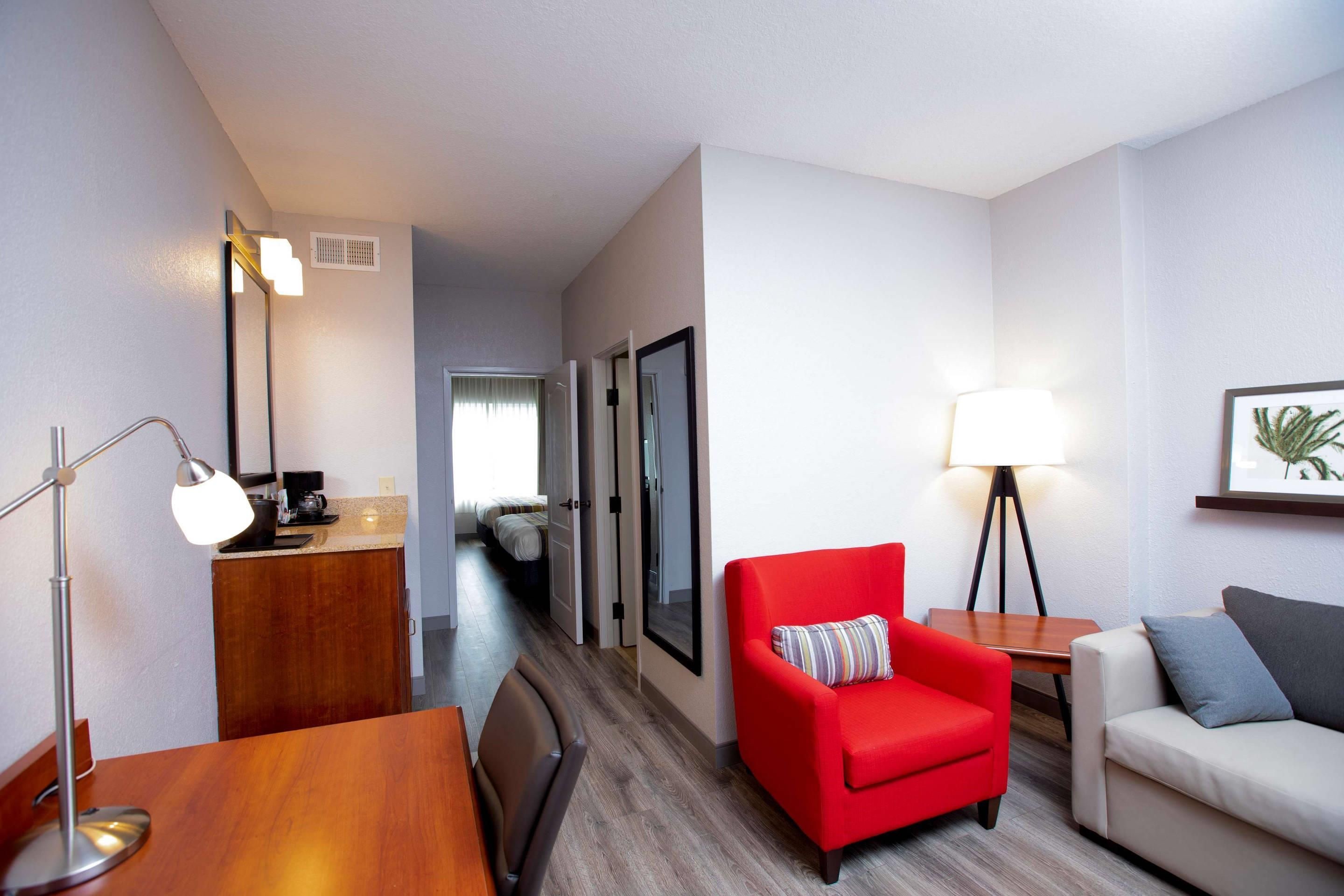 A hotel room with a wooden desk, a red armchair, a white sofa, and a floor lamp.