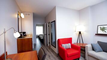 A hotel room with a wooden desk, a red armchair, a white sofa, and a floor lamp.