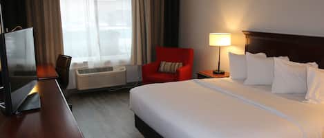 A hotel room with a large bed, a desk with a TV, a red armchair, and a window with curtains.