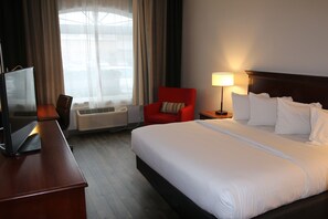 A hotel room with a large bed, a desk with a TV, a red armchair, and a window with curtains. - Country Inn & Suites by Radisson, Wilson, NC (Wilson)