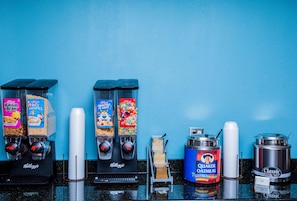 A breakfast bar with multiple Kellogg's cereal dispensers, a Quaker Oatmeal dispenser, and a grits dispenser. - Country Inn & Suites by Radisson, Wilson, NC (Wilson)