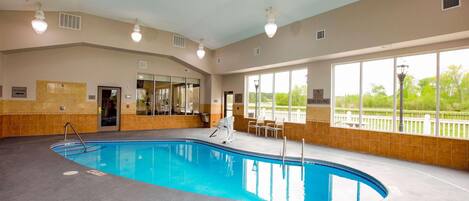 An indoor swimming pool with clear lanes, a lifeguard chair, and a view of the outdoors through large windows.