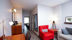 A hotel room with a wooden dining table, a red armchair, a white sofa, and a small side table with a lamp. - Country Inn & Suites by Radisson, Wilson, NC (Wilson)
