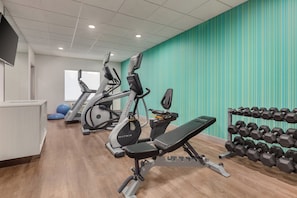 A gym with cardio machines, a bench, and a rack of dumbbells.