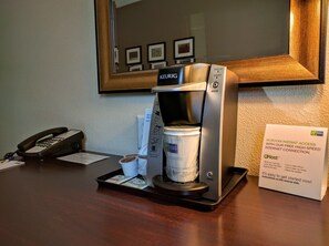 Une machine à café Keurig, avec une tasse de café et un plateau de dosettes de café, sur une table en bois.