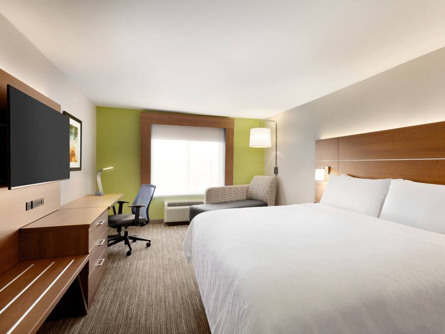 A hotel room with a large bed, a desk with a chair, a flat-screen TV, a window, and a lamp.