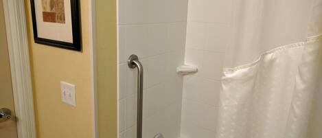 A bathroom with a shower, a handrail, and a framed picture on the wall.