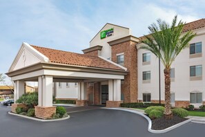 A hotel with a covered entrance, a brick facade, and a palm tree in the foreground. - Holiday Inn Express Hotel & Suites Merced by IHG (Merced)