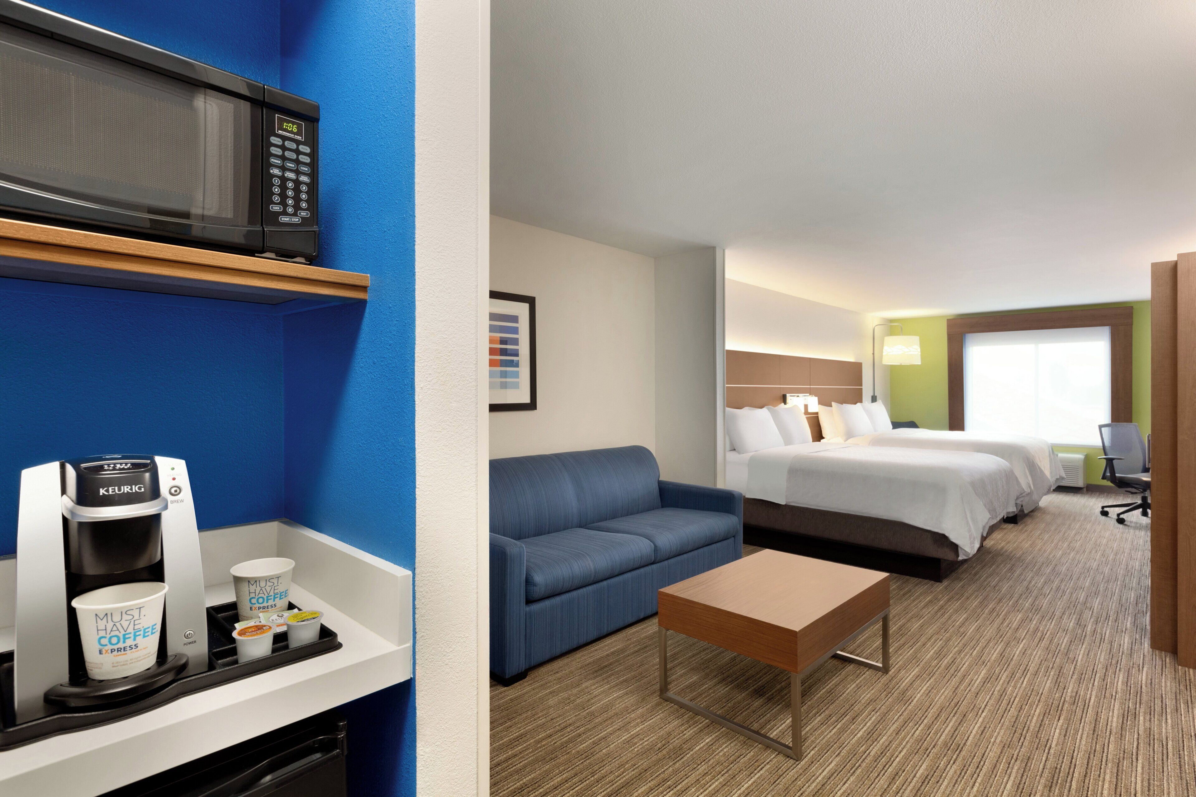 A hotel room with a kitchenette, a microwave, a coffee maker, a sofa, a bed, and a desk.