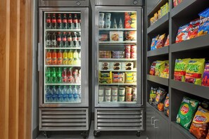 Two beverage dispensers stocked with various drinks and a snack shelf with chips and other snacks.